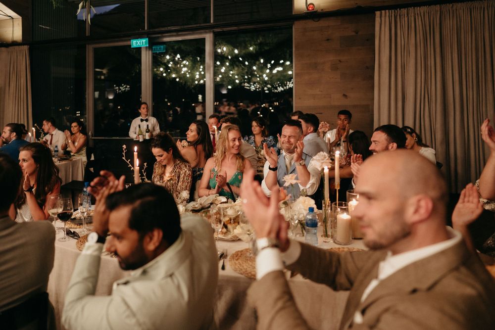 Wedding reception guests raise glasses in celebratory toast during evening dinner.