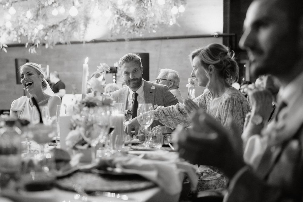 Black and white photo of wedding guests laughing during reception dinner.