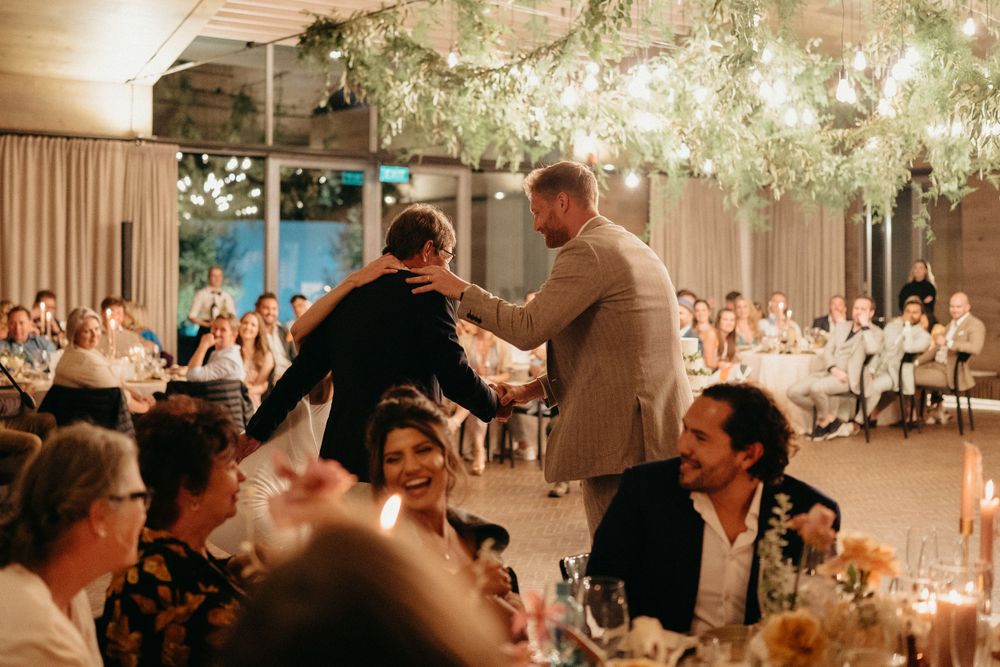 Wedding reception guests gathered in an elegant venue with hanging floral arrangements and candlelit tables.