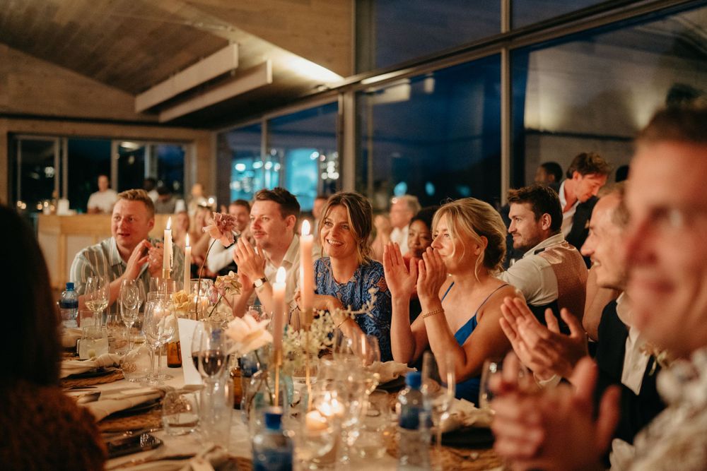 Guests clapping and celebrating at a candlelit wedding reception dinner table.