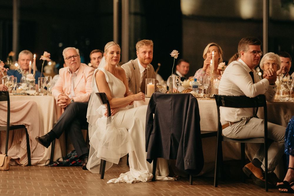 Wedding party seated at dining tables during reception celebration with warm ambient lighting.