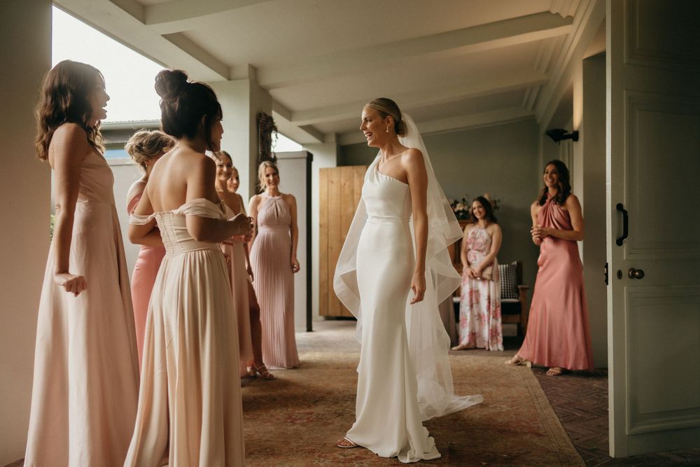 Wedding party gathering in a hallway with bridesmaids in pink dresses.