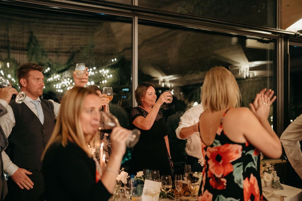 Wedding guests dance and celebrate at an evening reception with string lights overhead.