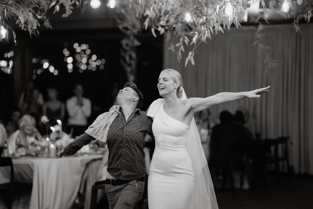 A bride in white dress dances joyfully with her partner under ambient lighting at wedding reception.