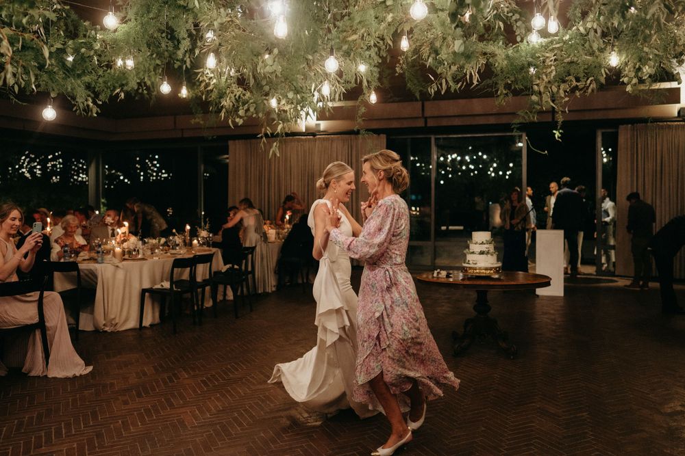 Wedding guests dance beneath twinkling lights and greenery at an elegant evening reception.