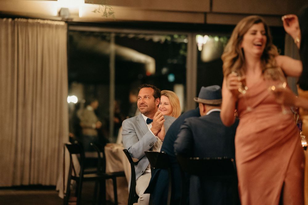 Wedding reception guests enjoying entertainment and conversation in dimly lit venue.