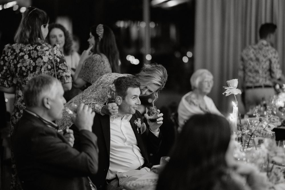 Black and white photo of wedding guests enjoying speeches during an evening reception.