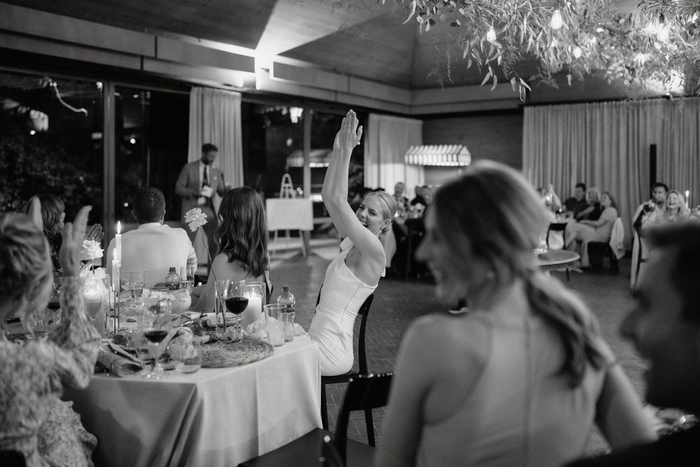 Wedding guests raising their hands in celebration during a black and white reception moment.