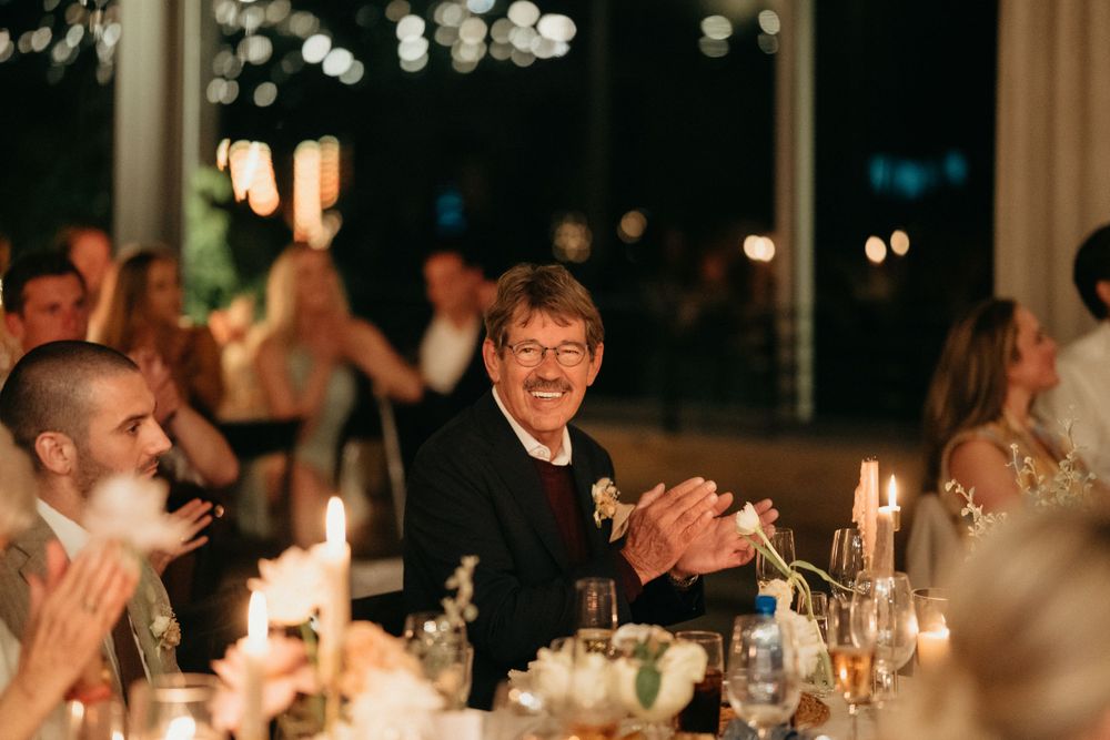 Wedding guests applaud during a candlelit evening reception celebration.