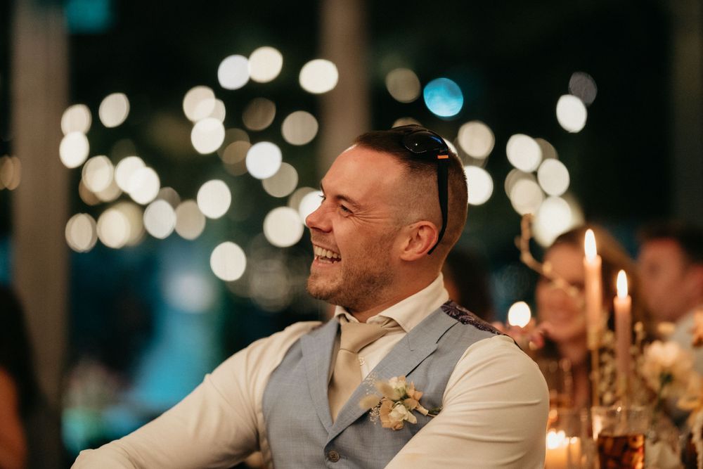 Guest in a light gray vest enjoys a candlelit wedding reception with bokeh lights in background.