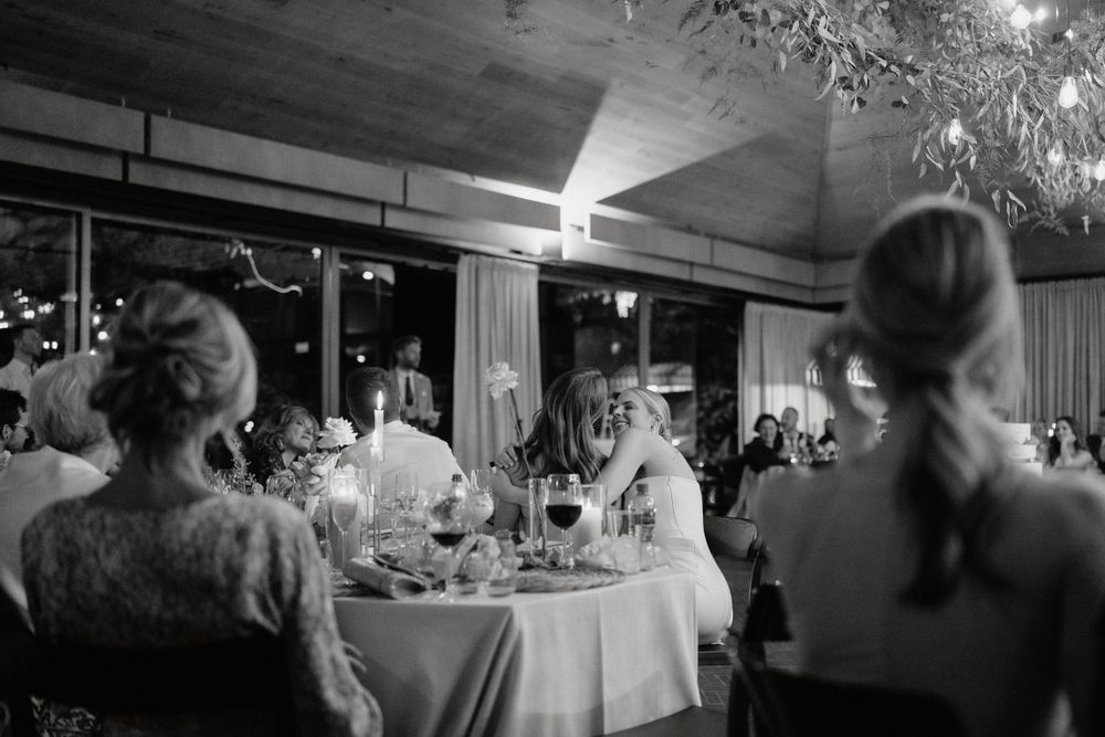 Reception guests seated at tables with elegant decor and hanging greenery in black and white.