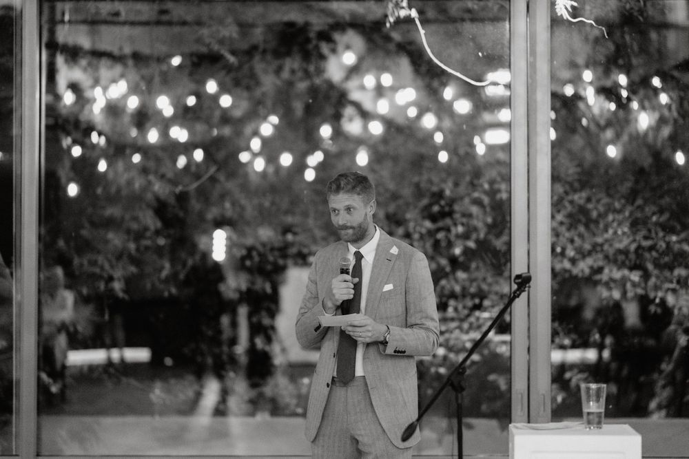 A speaker delivers remarks at an outdoor evening event with twinkling lights in the background.