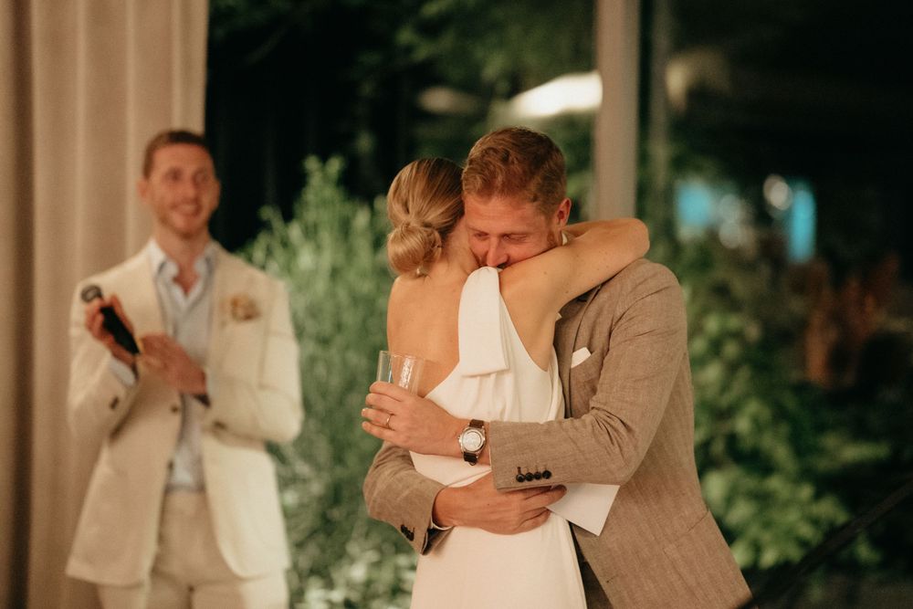 A couple shares an intimate embrace during their wedding reception outdoors at dusk.