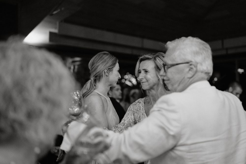 Black and white candid shot of people dancing together at what appears to be a wedding celebration or social event.
