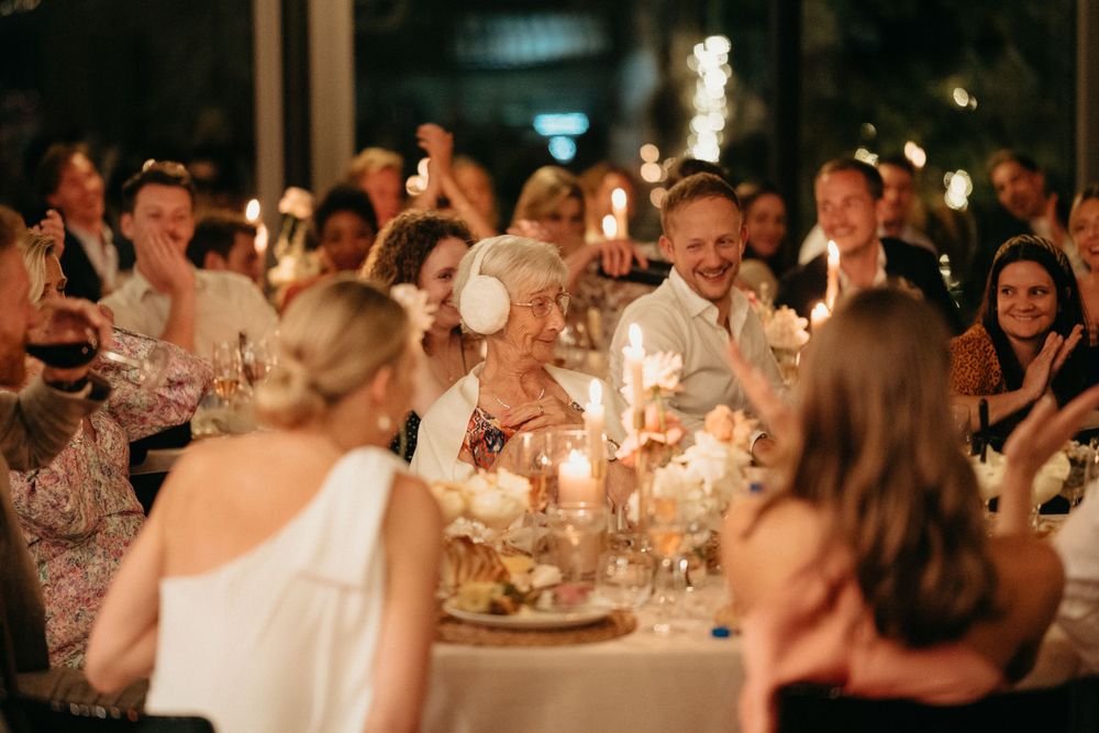 Wedding reception guests gather around elegantly decorated tables with glowing candles creating an intimate atmosphere.