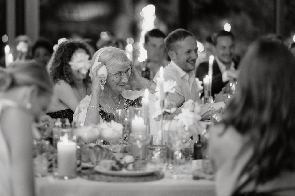 Black and white photo of wedding guests dining at candlelit tables during evening reception.