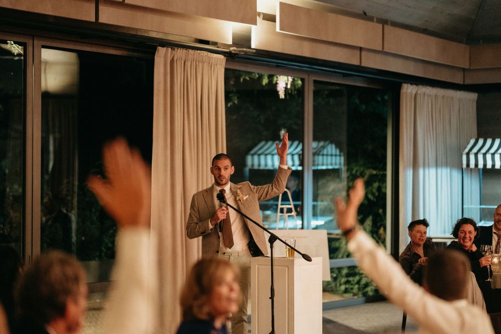 Speaker addresses wedding guests during reception as hands raise in celebration.