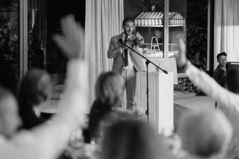 A speaker addresses an animated crowd from a podium while audience members raise their hands in a black and white photo.