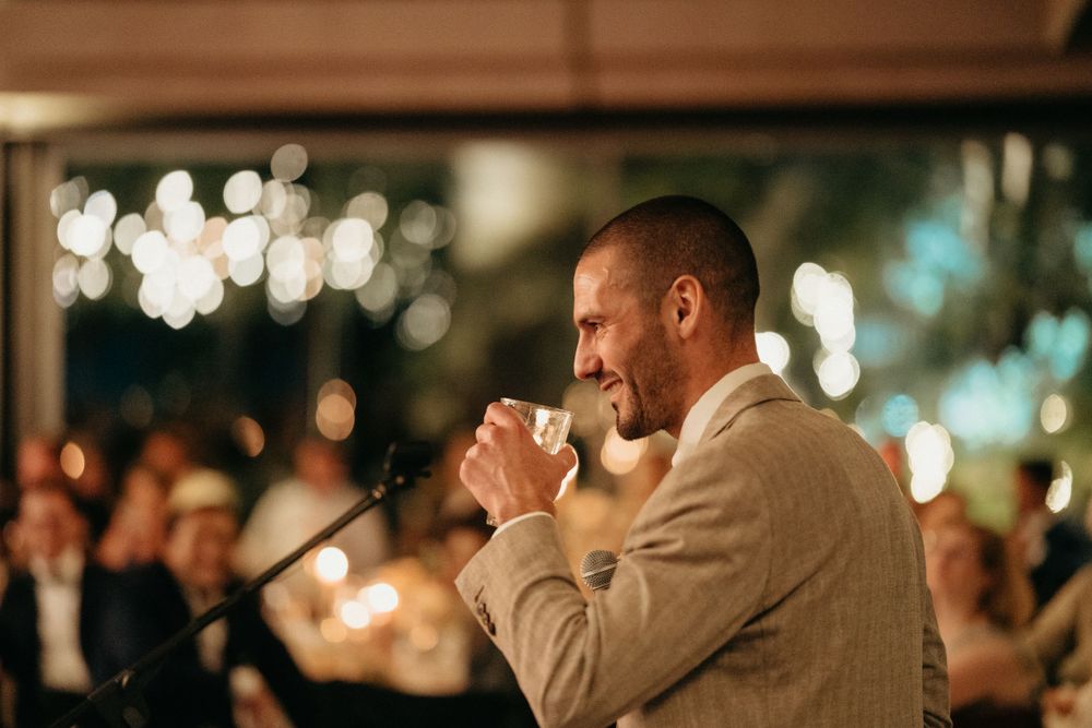 Guest gives emotional speech at evening wedding reception with bokeh lights.