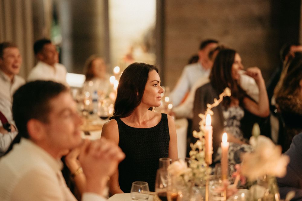 Wedding reception guests enjoying dinner and conversation under warm lighting.