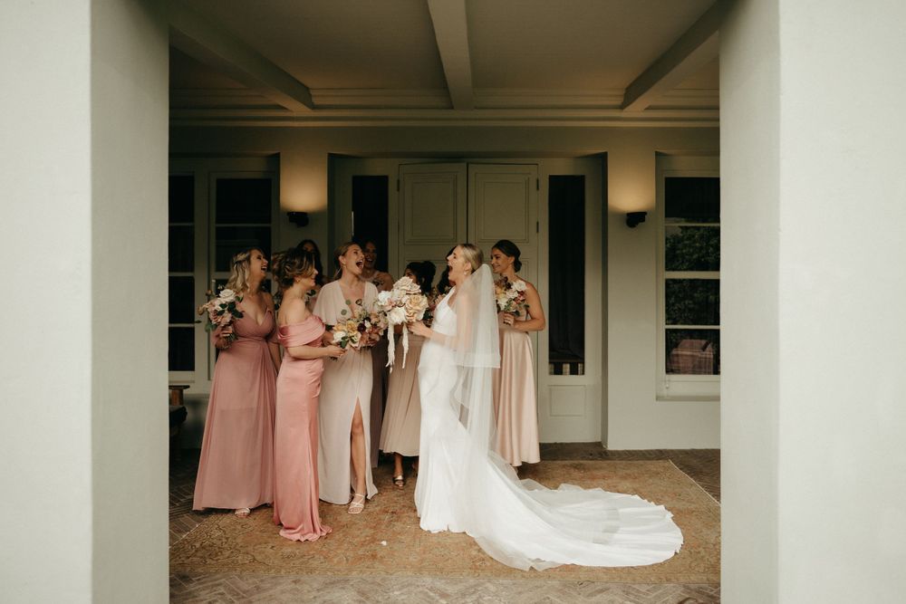 A wedding party gathers under a covered walkway with the bride in a flowing white gown.