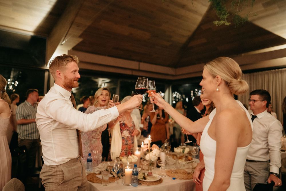 Newlyweds share a celebratory toast during their wedding reception under wooden beams.