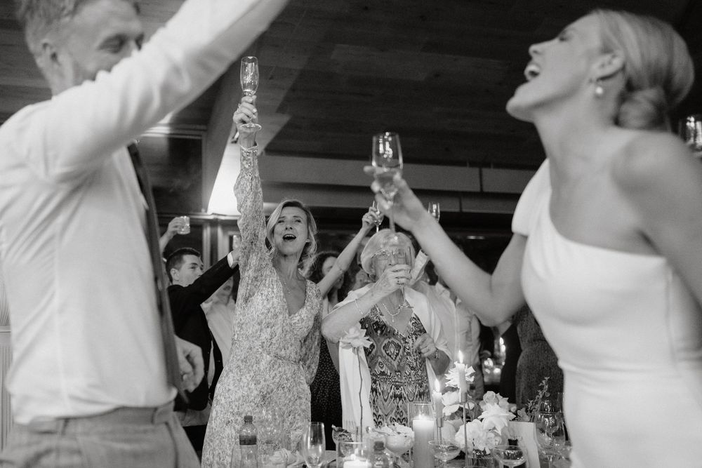 Wedding party toasting and celebrating with raised glasses in black and white photography.