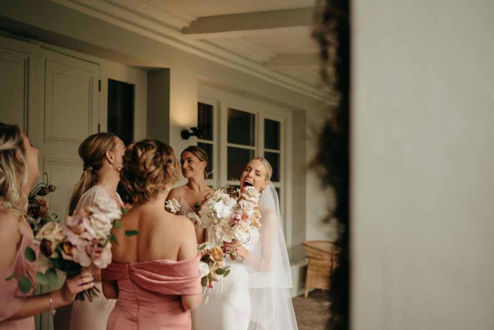 A bridal party gathering with bouquets in a sunlit room.