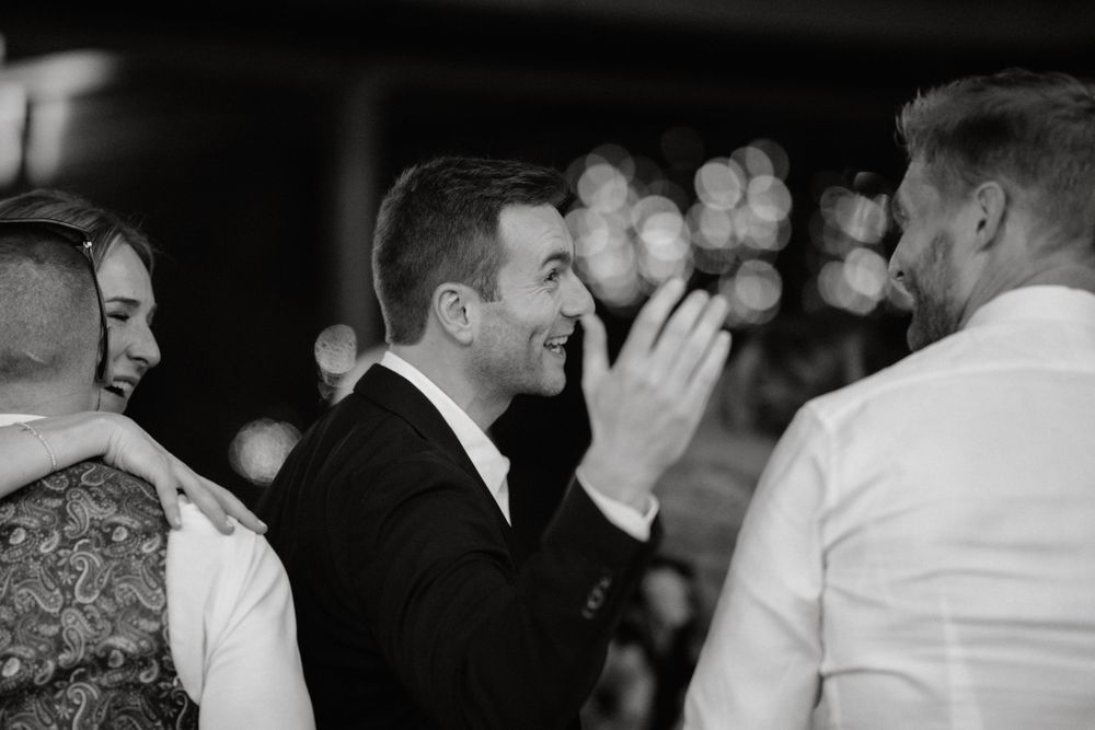 Black and white photo of joyful guests sharing laughter at an indoor evening celebration.