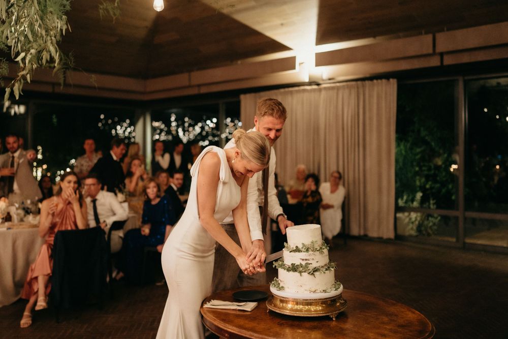 Newlyweds cut their elegant white wedding cake together during the reception celebration.