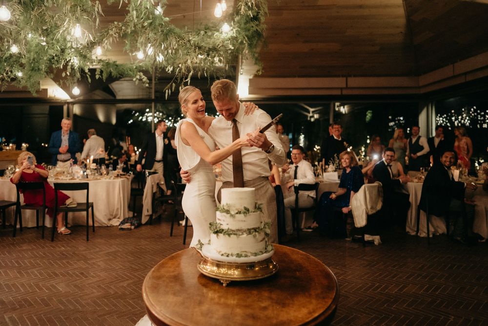 Couple cuts their elegant white wedding cake together during an evening reception.