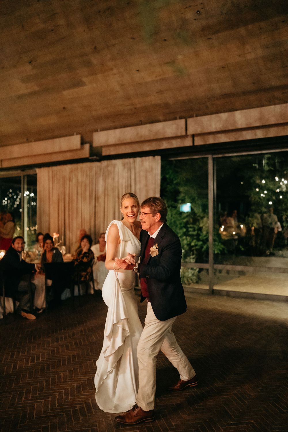 Couple dancing on wooden floor during evening wedding reception with warm lighting.