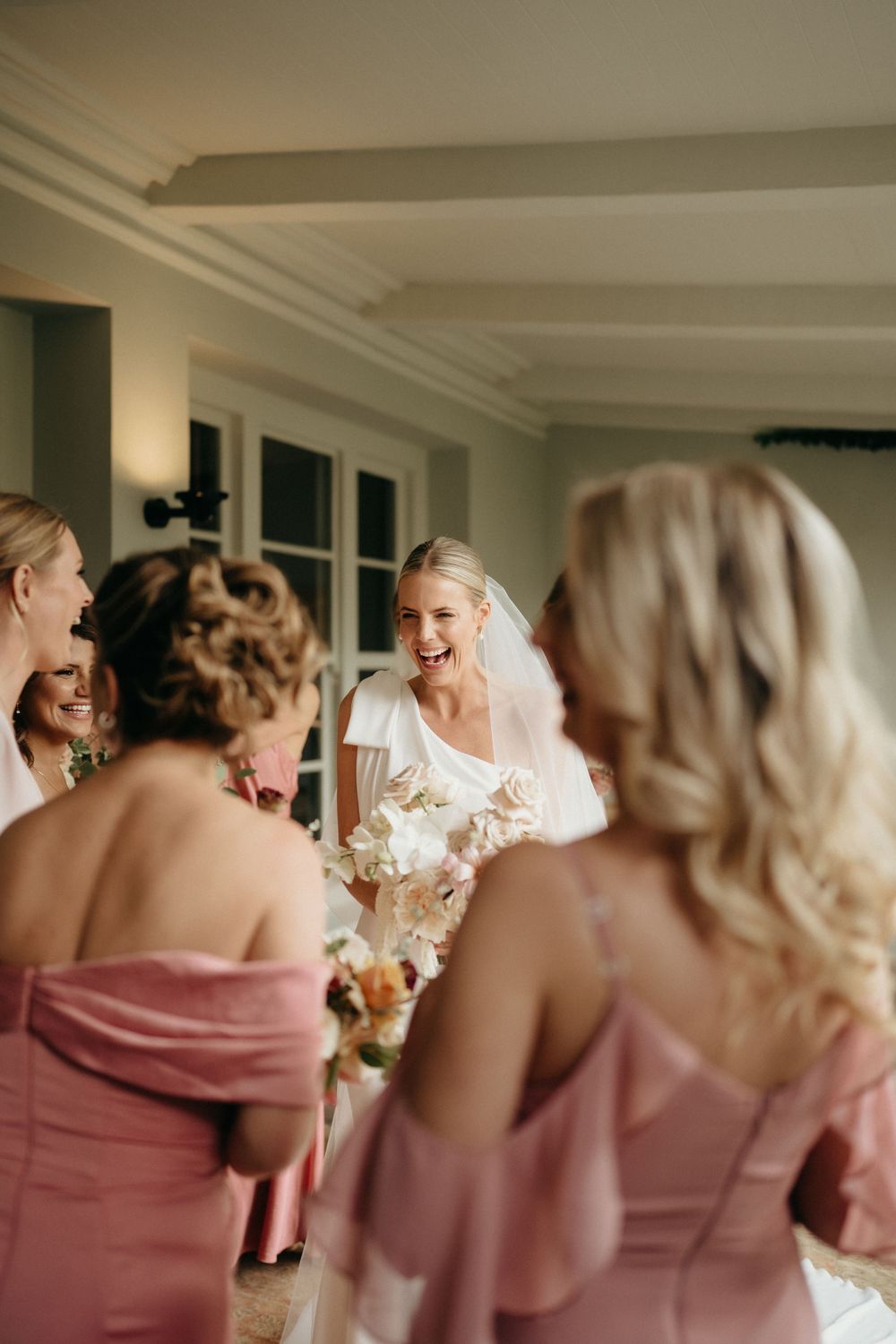 Bridesmaids in pink dresses share a joyful moment during wedding preparations.