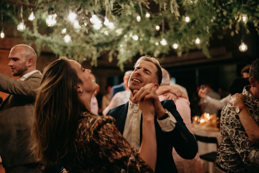 Wedding guests laughing and dancing together under decorative lights.