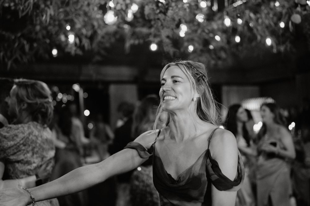 Black and white photo of guest dancing joyfully under twinkling lights at reception.