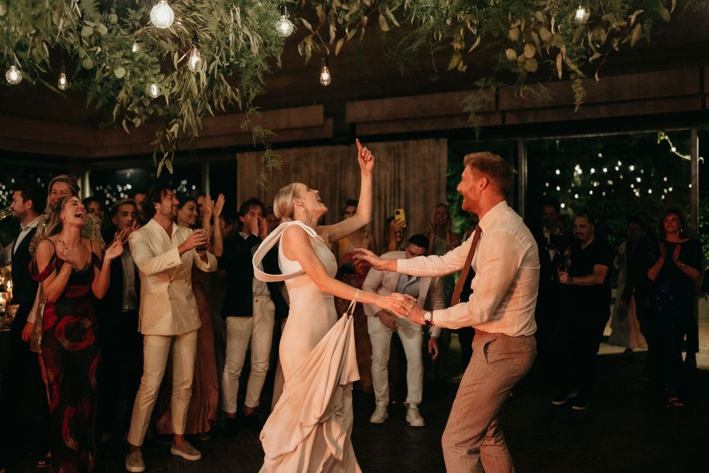 Wedding celebration showing energetic dancing under rustic wooden beams and hanging greenery.