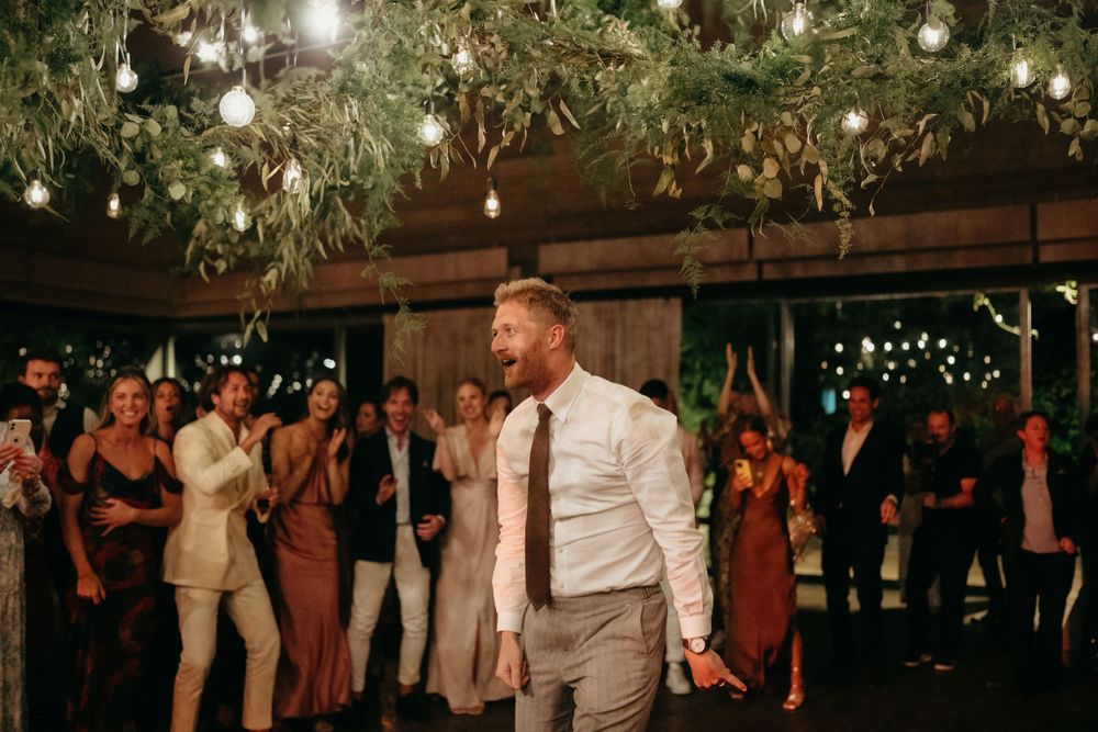 Wedding guest dances enthusiastically under hanging greenery and string lights.