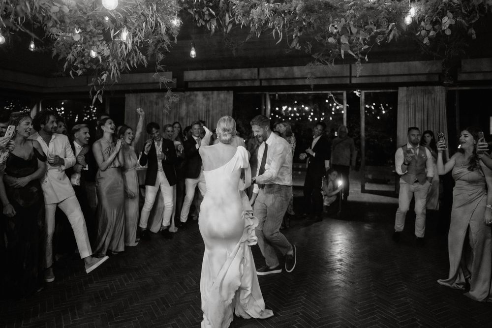 Guests surround a dancing couple at an outdoor evening wedding reception under twinkling lights.