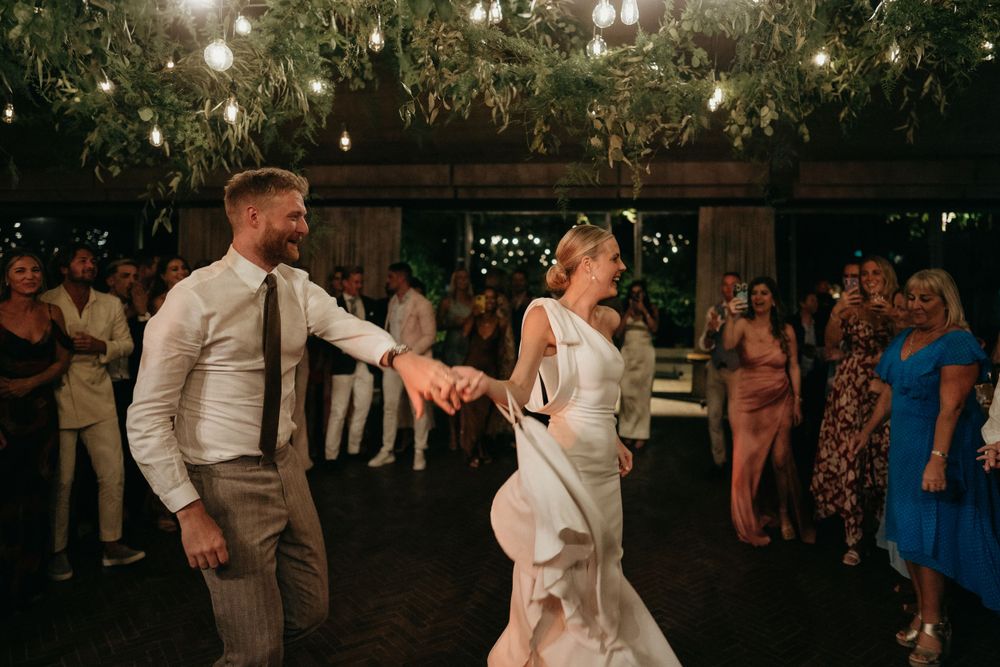 Couple performs romantic dance moves under decorative lights and greenery.