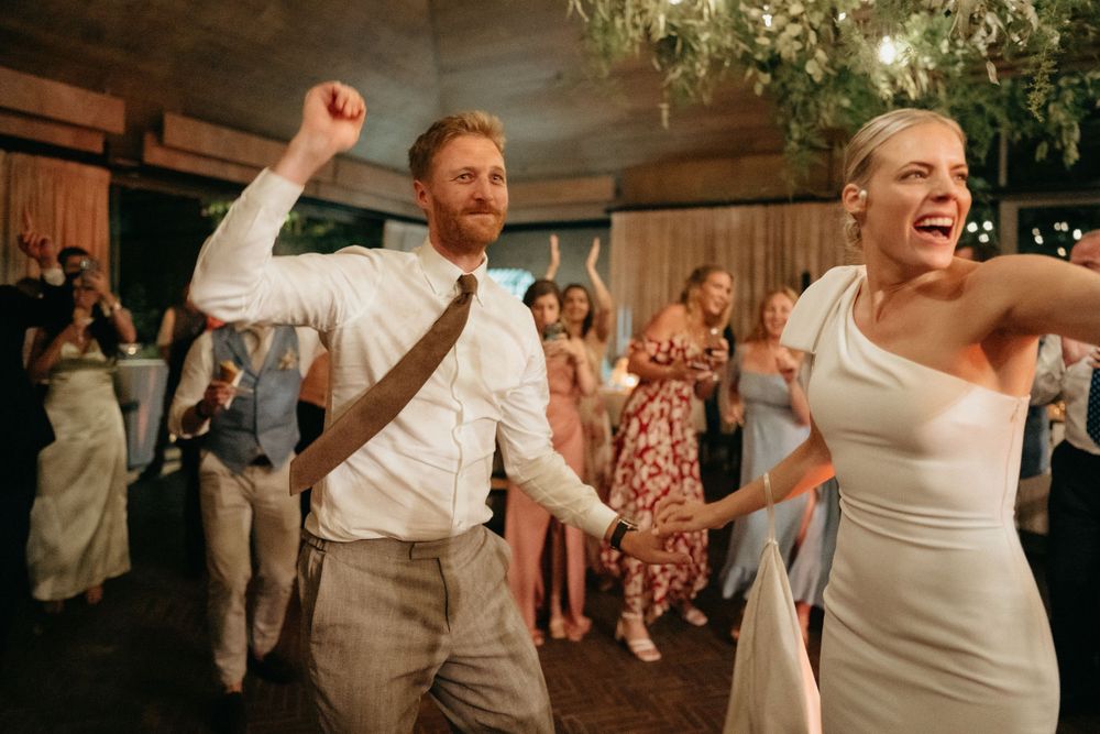 Celebratory dancing at a reception under decorative greenery and warm lighting.