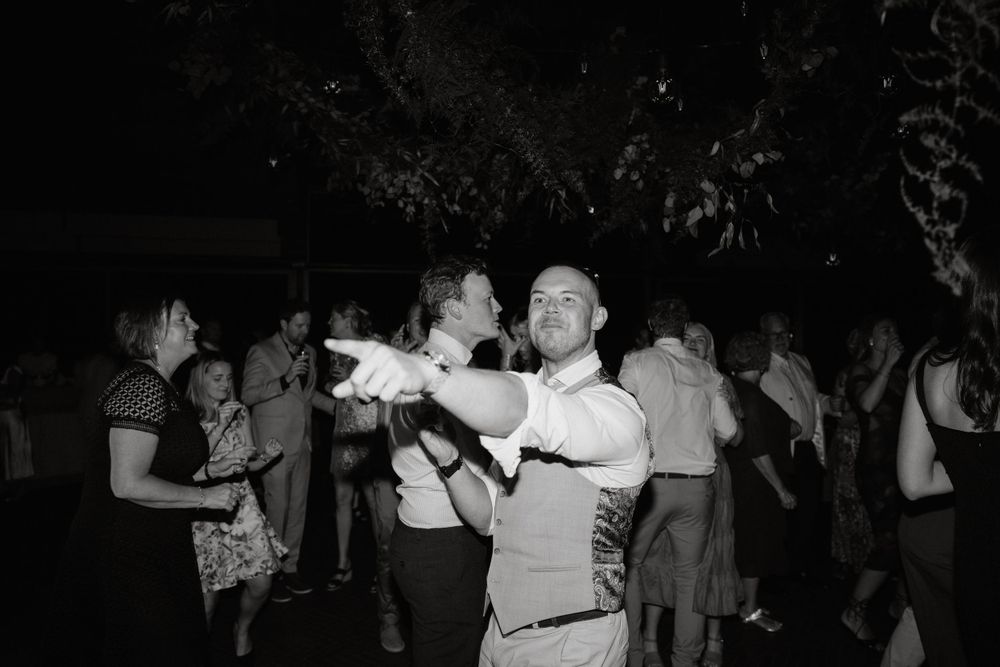 Black and white photo of wedding guests dancing at night under outdoor lighting.