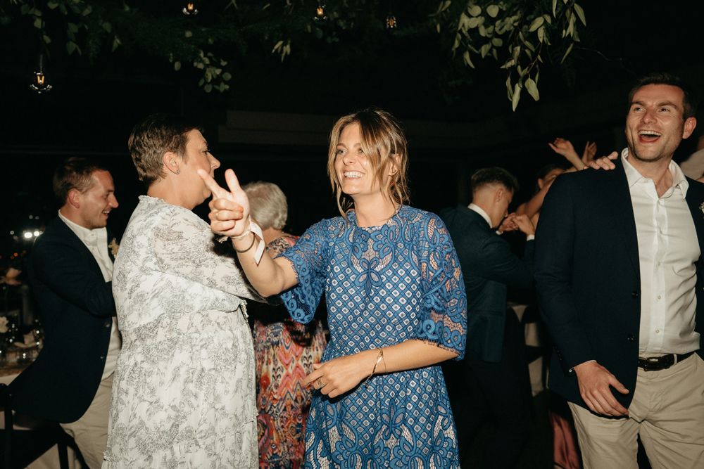 Wedding guests laughing and dancing at outdoor evening reception.