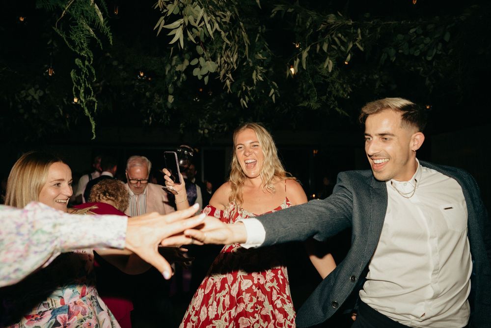 People dancing and reaching out to each other at a nighttime outdoor party with trees and festive atmosphere.