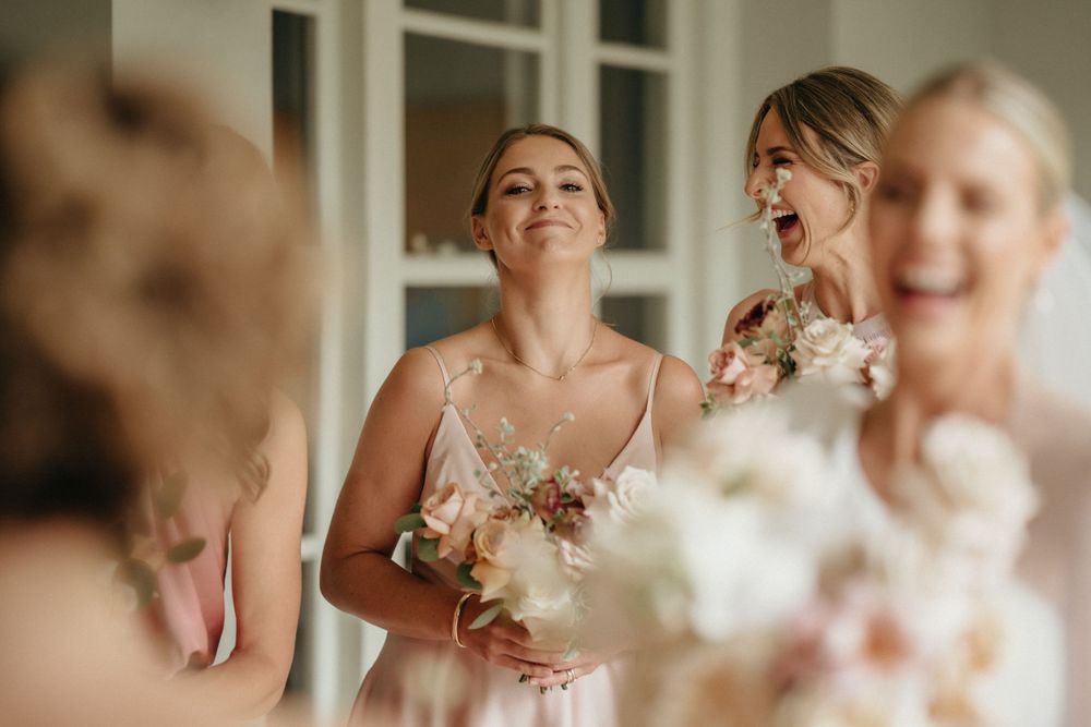 Bridesmaids in pink dresses share a joyful moment while getting ready for the wedding.