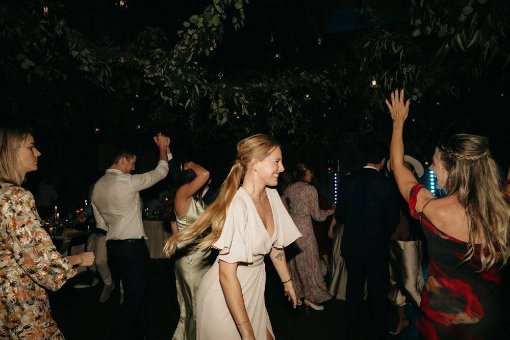 Wedding guests dancing together at night under trees at outdoor reception.