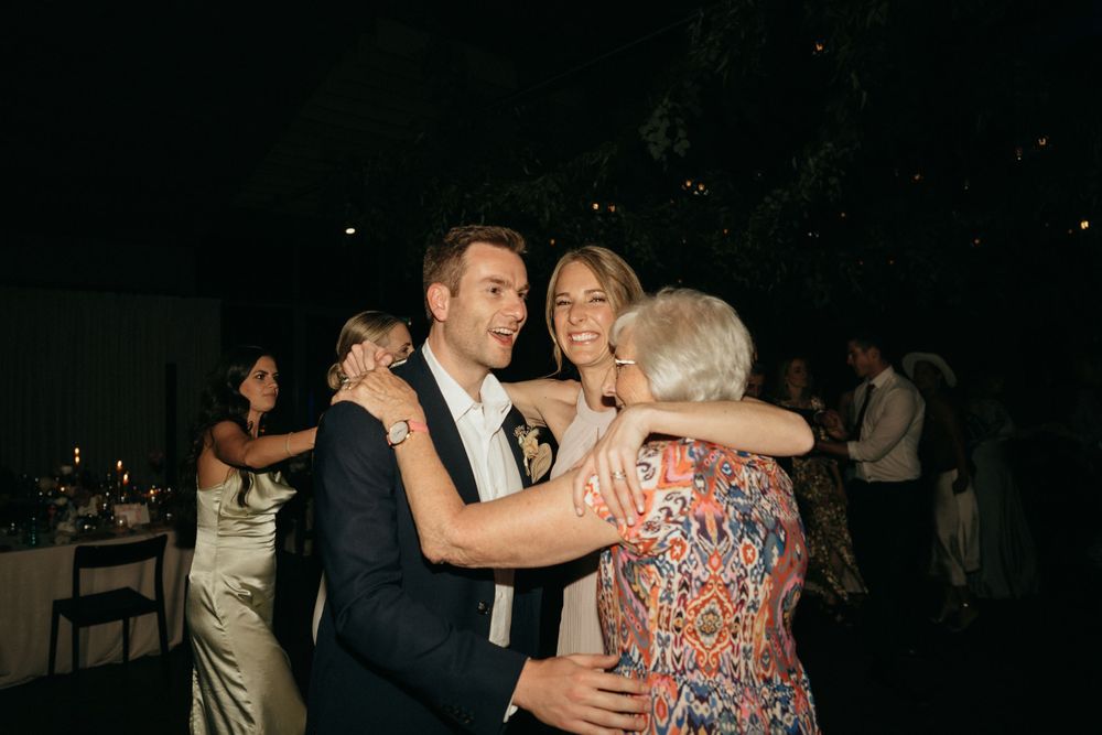 Three people share an emotional embrace while dancing at an evening wedding reception.