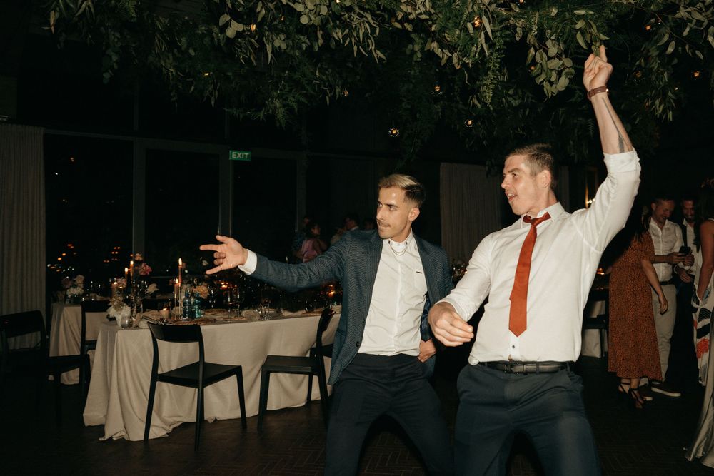 Two people dancing enthusiastically at an evening outdoor reception with tables in background.