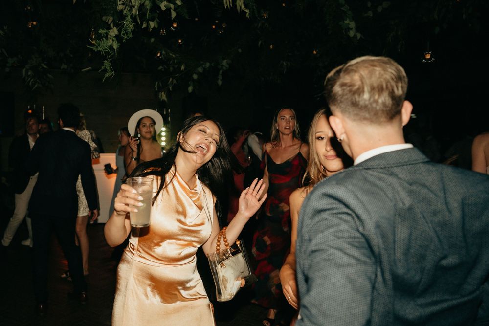 Party guests dancing and laughing together at a nighttime celebration with festive lighting.
