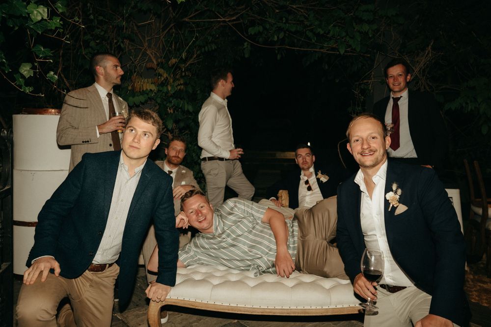 Wedding party guests pose casually on outdoor furniture during evening reception.