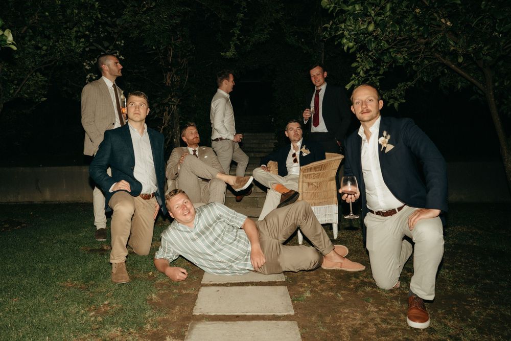 Groomsmen posing playfully on garden path during evening wedding celebration.